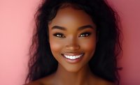 Young African American woman with radiant smile and natural wavy black hair against pink background, expressing joy and confidence in close-up portrait.