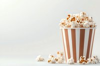 Fresh popcorn in striped brown and white paper container with scattered kernels on light background, minimalist cinema snack composition.