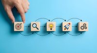 Business strategy concept with hand placing wooden blocks showing target, search, idea, growth and teamwork icons on blue background.