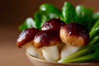Fresh shiitake mushrooms with green lettuce leaves on wooden plate, macro food photography with soft natural lighting and shallow depth of field.