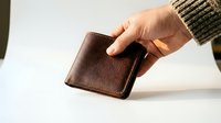 Hand holding a brown leather bifold wallet against a light background, showcasing craftsmanship and texture for fashion or retail use.