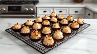 Homemade chocolate macaroons with toasted coconut flakes cooling on black wire rack in bright modern kitchen, selective focus on sweet treats.