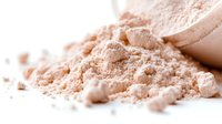 Loose cosmetic powder in soft beige tone with scattered particles on white background, used for makeup application and skin tone evening.