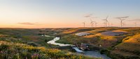Wind turbines generating renewable energy across rolling hills with winding river at golden hour sunset creating sustainable power landscape for environmental projects.