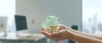 Hands holding glowing green recycling symbol with leaf icon in modern office environment, representing sustainability, eco-friendly business practices and environmental responsibility.