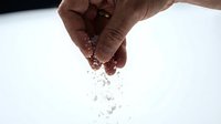 Close-up of hand sprinkling salt or seasoning powder over white surface, cooking ingredient preparation for culinary use.