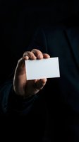Professional businessman hand holding blank white business card in dark moody lighting for corporate branding and networking presentations.