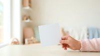 Young woman with medium skin tone wearing a pink ribbed sweater holding a blank white card in her hand, ideal for greeting cards, invitations, announcements, and promotional messaging designs.