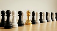 Golden chess pawn standing out among black and white pawns on wooden board, representing leadership, uniqueness, and strategic thinking in business concepts.