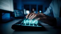 Businessman hand pressing glowing approved button on digital keyboard in modern office workspace with computer screens, symbolizing business approval and digital confirmation process.