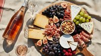 Rosé wine with charcuterie board featuring cured meats, aged cheeses, fresh figs, grapes, nuts and berries on wooden surface for entertaining and gatherings.