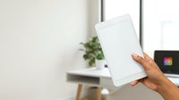 Woman holding blank tablet device with empty screen in modern office workspace with natural light and green plant decoration.