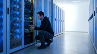 IT technician maintaining server equipment in modern data center with blue LED lighting and white corridor for technology infrastructure concepts.