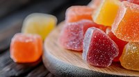 Colorful sugar coated gummy candies on wooden surface in macro shot, showing texture and crystalline coating. Sweet treats with red, orange and yellow colors.