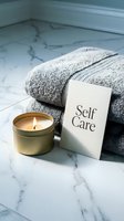 Self care concept with lit candle, folded gray towels, and card on marble surface for wellness, spa, and relaxation themes.