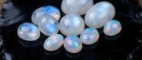 Collection of polished opal gemstones displaying iridescent fire and rainbow colors on dark surface for jewelry making and mineral collecting purposes.