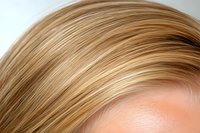 Close-up view of blonde hair strands showing natural highlights and texture against soft blurred background, demonstrating professional hair coloring and styling techniques.