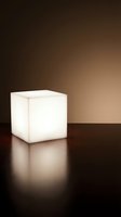 Glowing white cube lamp on dark surface with warm brown gradient background, modern minimalist lighting design for interior decor.
