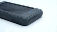 Portable solar charger with dark gray rubberized casing and integrated solar panel on white background for tech product photography and renewable energy concepts.
