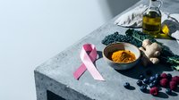 Pink ribbon symbol with turmeric powder, blueberries, kale and olive oil on concrete surface for cancer awareness and healthy nutrition concept.