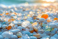 Smooth pebbles and sea glass on beach at sunset with golden bokeh light effects, close-up macro photography showing natural texture and warm evening glow.