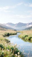 Serene mountain valley landscape with meandering stream flowing through lush meadow, misty peaks in background, ideal for nature and travel projects.