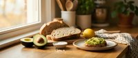 Fresh avocado toast with herbs on rustic wooden table by sunny window. Healthy breakfast scene with artisan bread, lemon, and kitchen plants.