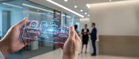 Hands holding smartphone displaying augmented reality interface with digital icons and data visualization in modern office environment with blurred colleagues in background.