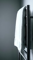 White towel draped over black heated towel rail against neutral gray background, suitable for bathroom, spa, and home decor design projects.