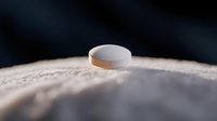 White pharmaceutical pill tablet on wooden surface with dramatic lighting and dark background for medical healthcare concepts.