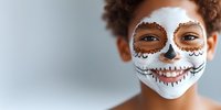 Young woman with curly afro hair wearing traditional Day of the Dead sugar skull face paint makeup in white and brown colors against light background.