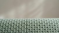 Knitted fabric texture in soft green and white colors with detailed stitch pattern against neutral background for textile and craft projects.