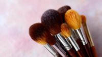 Professional makeup brushes with soft brown and golden bristles arranged in fan composition against blurred pink background, cosmetic tools for beauty artists.