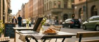 Outdoor café table with fresh croissant and coffee cup on sunny urban street, ideal for restaurant, bakery, and hospitality marketing.
