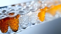 Macro shot of condensation droplets on glass surface with amber liquid behind, creating abstract pattern of water drops and bokeh effect. Refreshing beverage background.