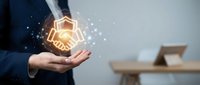 Businessman holding glowing handshake hologram with digital network connections representing partnership and collaboration in modern office environment.