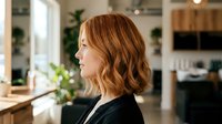 Professional businesswoman with wavy auburn hair in profile view standing in modern bright kitchen interior with natural lighting.