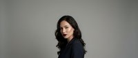 Professional young Hispanic woman with dark wavy hair in black blazer against neutral background for business and corporate marketing materials.