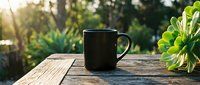 Black coffee mug on rustic wooden table with green succulent plant in sunny garden setting with natural bokeh background for morning relaxation concepts.