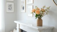 Elegant peach roses and white wildflowers in a ceramic vase on a marble mantel, soft neutral interior with framed art on the wall.