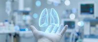 Hand holding glowing holographic lungs in modern medical facility representing respiratory health technology and healthcare innovation.