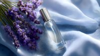 Fresh lavender flowers next to glass perfume bottle on flowing blue silk fabric with soft shadows and natural light for cosmetic and fragrance marketing.
