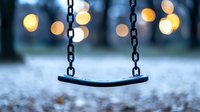Empty swing with blurred bokeh lights in background creates nostalgic winter mood, frozen ground beneath shows seasonal atmosphere. Loneliness concept.