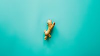 Small golden ginger cat figurine on vibrant turquoise background with soft shadow, minimalist composition for modern design and creative projects.