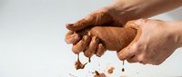 Hands of Caucasian male holding and crumbling brown soil or earth against white background, suitable for agriculture, gardening, environmental and farming concepts.