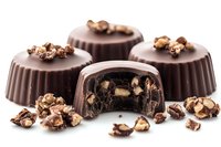 Dark chocolate pralines with nuts and caramel filling, one cut in half showing rich interior texture, scattered crushed nuts on white surface, macro food photography.