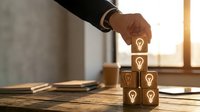 Professional businessman stacking wooden blocks with lightbulb icons representing creative ideas, innovation and business growth strategy in modern office.