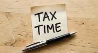 Tax time reminder note with pen on wooden desk for accounting and financial planning preparation during filing season.