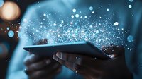 Magical sparkles and glowing particles emerging from digital tablet held in hands against blue background, representing digital transformation and innovation.