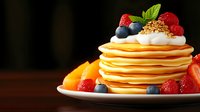 Stack of fluffy pancakes topped with fresh berries, whipped cream, granola and maple syrup on white plate against dark background, morning breakfast setup.